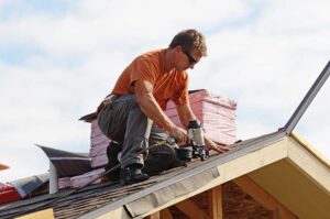 A worker examining torn shingles and damaged flashing on a residential roof after a windstorm.