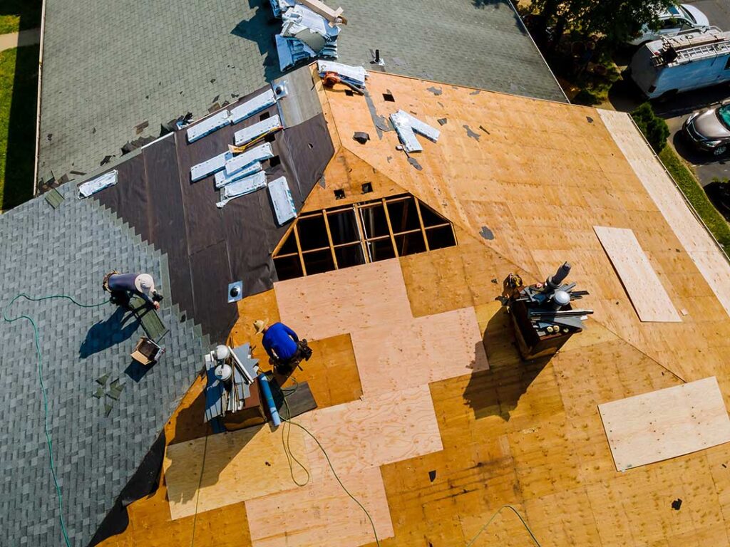 A homeowner reviews roof condition with an inspector beside a snow-dusted suburban house.